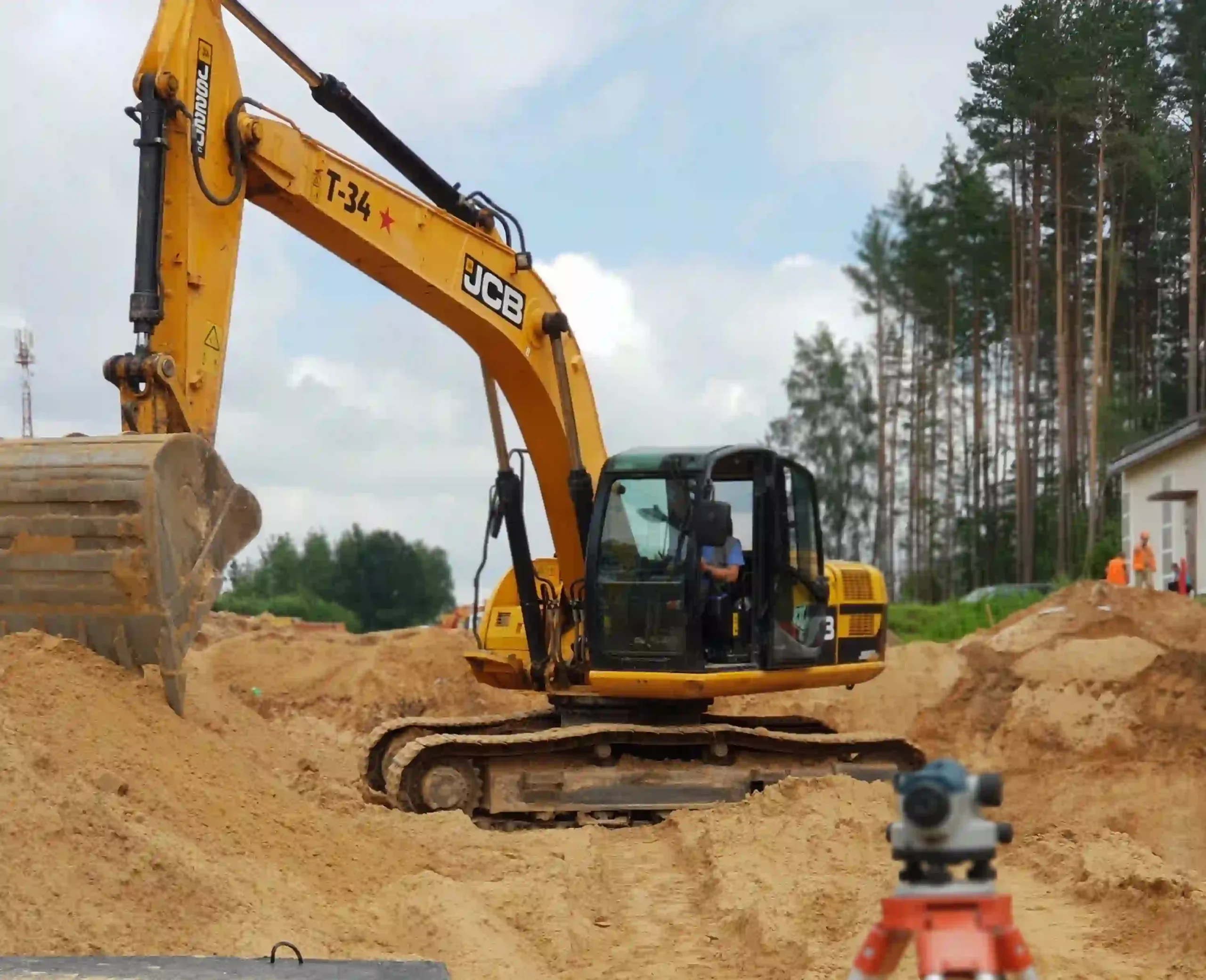 Прокладка сетей канализации в парке «Великий камень» — экскаватор JCB разрабатывает траншею, нивелир на переднем плане